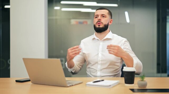 Bearded man in white shirt waving hands and gasping for air during panic attack at desk. Scared male executive experiencing anxiety, fear or emotional breakdown at office.