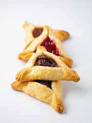 Pile of traditional triangular hamantaschen cookies with different fillings, filled with poppy seed and apricot jam, arranged on a white background