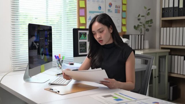A woman is sitting at a desk with a computer monitor and a keyboard. She is using a stylus to draw on a piece of paper