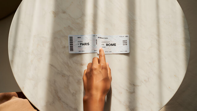 ​A high-angle close-up shot of a thumb pressing down on a small printed ticket or boarding pass placed on a smooth surface under warm light.