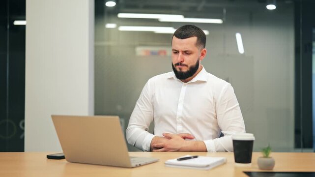 Businessman experiences abdominal pain while concentrating on laptop work. Unwell feeling disrupts productivity at office desk. Pain causes distress, affecting focus and well-being.