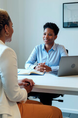 Vertical shot of Black young adult businesswoman meeting female client across desk, discussing work goals and planning strategy. Ideal for consulting, recruitment, coaching, or HR services