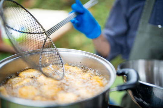 Street food deep fry hot oil frying pan cook chef glove outdoor market crispy snack Street food chef using wire skimmer over hot oil large pot while deep fry snack bubbles and sizzles outdoor