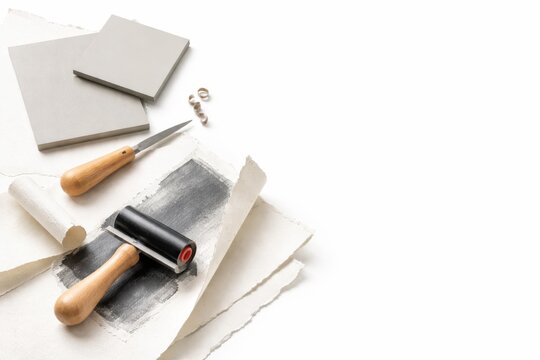 Modern printmaking still life with linocut blocks wooden brayer deckled papers and ink traces isolated on white background