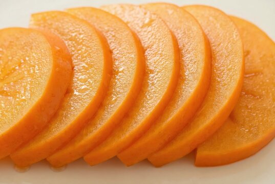 Freshly sliced persimmons arranged in a circular pattern showcasing their vibrant orange hues and glossy texture creating a visually appealing composition and healthy snack idea