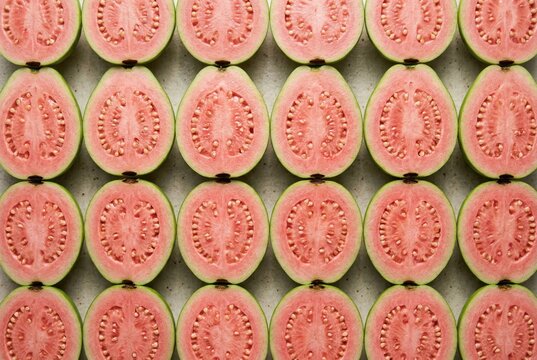 Vibrantly arranged guava slices showcasing intricate seed patterns and succulent pink flesh create a compelling visual narrative on a neutral backdrop highlighting abundance and freshness