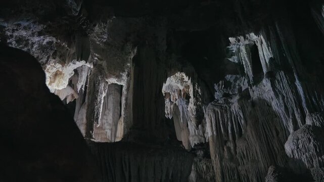 Exploring a dark cave with flashlights reveals stunning stalactites and natural rock formations. Dramatic underground scenery highlights geological textures and mysterious beauty