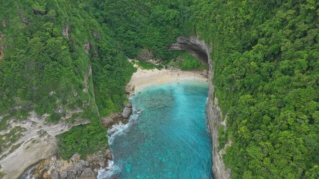 Dramatic aerial view flying over a remote cove known as sunfish beach in nusa penida, bali, showing turquoise water and lush cliffs