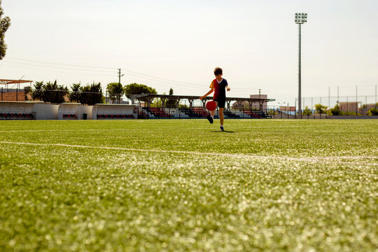 Young boy playing football on a green artificial turf field