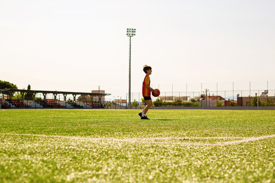 Young boy playing football on a green artificial turf field