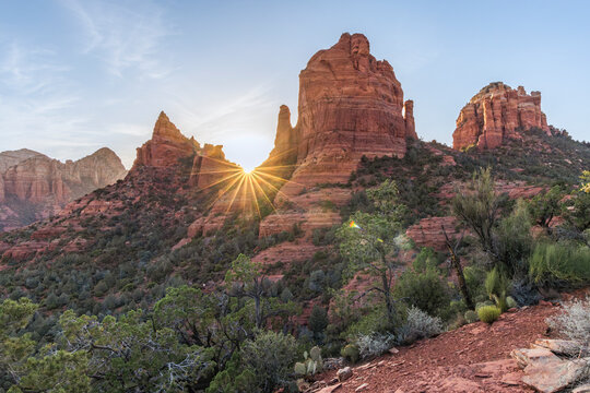 Starburst sun setting behind red rock landscape