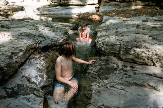 Children sitting in small waterfall in rocky stream