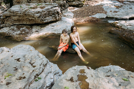 Children sitting on rock in scenic stream in summertime