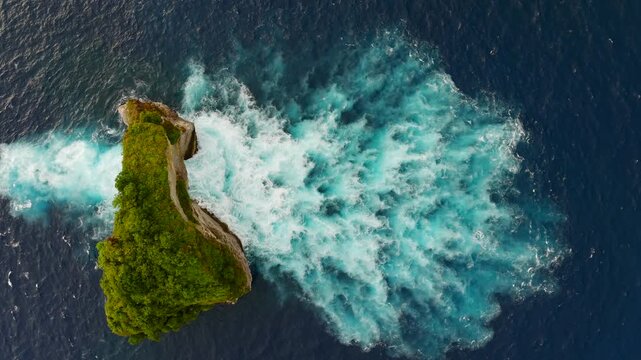 Top down aerial drone view of ocean waves crashing through natural sea arch, abstract water texture and rocky island, Bali, Indonesia.