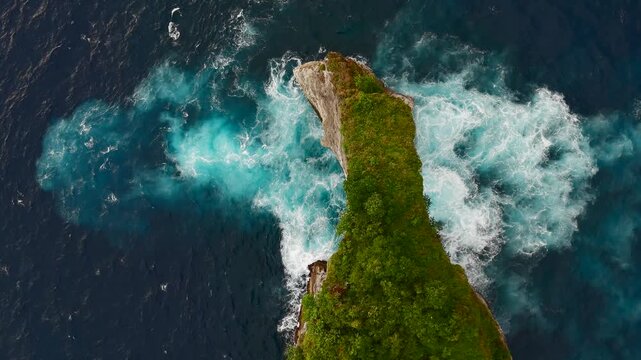 Top down aerial view of ocean waves crashing around rocky island and natural sea arch, abstract water texture, Bali, Indonesia.