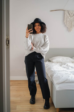 Stylish woman taking mirror selfie in casual outfit inside modern bedroom