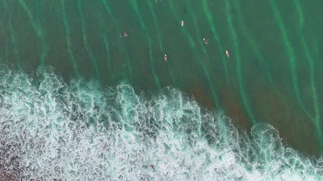 Aerial drone shot flying parallel to surfers riding waves near dramatic rocky cliffs in Bali, Indonesia. Dynamic action scene capturing the thrill of surfing in crystal clear ocean water