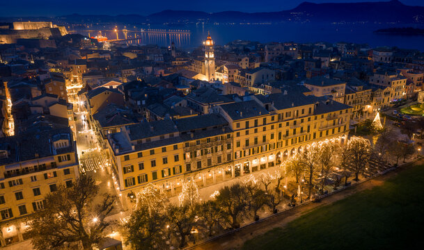 Panoramic aerial night view of Corfu Old Town featuring the Old Fortress, Liston promenade, and Saint Spyridon tower illuminated
