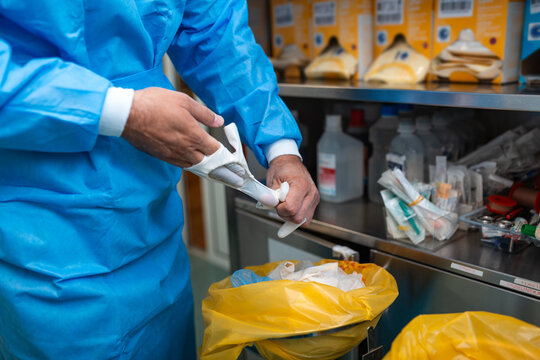 Medical professional removing sterile surgical gloves after operation. Surgeon taking off protective rubber gloves in hospital operating room near medical waste bin. Hygiene and safety protocols.