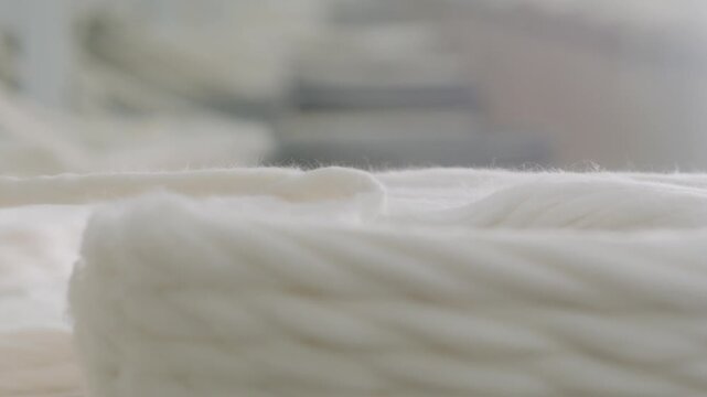 Close-up of cotton sliver production in a textile spinning mill. Detailed view of raw white cotton fibers being processed and coiled during the carding stage of garment manufacturing