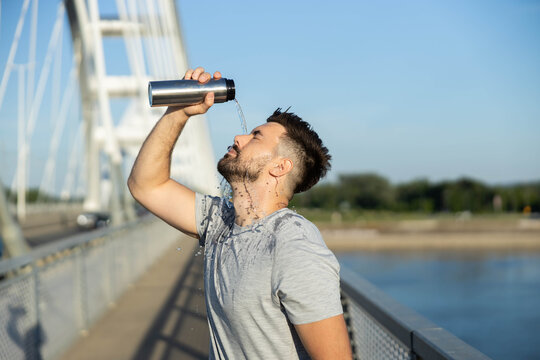 Young man pouring water over his face and head on a bridge, feeling refreshed and cooling down from the heat