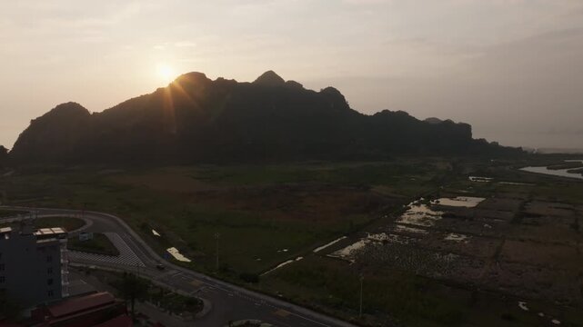 Cat Ba Vietnam drone glide over village rooftops and a highway curve, framed by limestone karst hills and wetlands.
