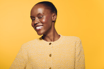 Obraz premium Smiling African woman with dark skin wearing a yellow sweater poses against a bright yellow background. Concept of happiness, beauty, confidence, and fashion portrait.
