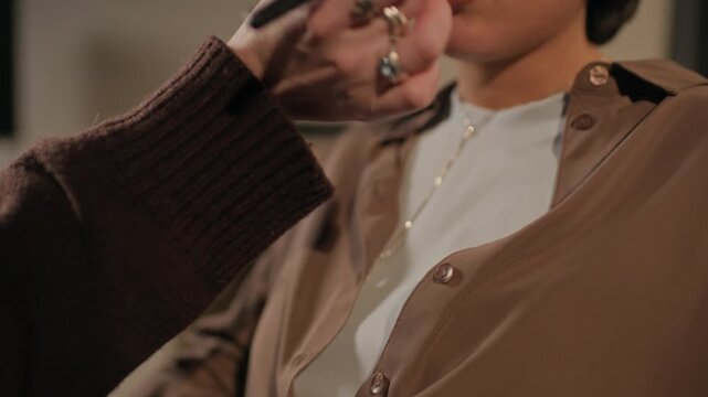 Tilt up shot of multiethnic young adult female comedian revising speech on clipboard while makeup artist applying powder in dressing room before stand up comedy show