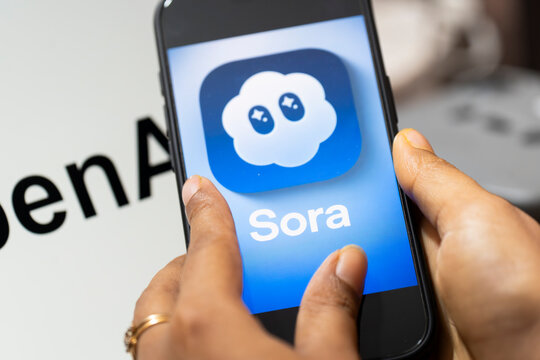 In this photo illustration, a smartphone displays the Sora AI logo in landscape orientation, with the OpenAI logo visible in the background