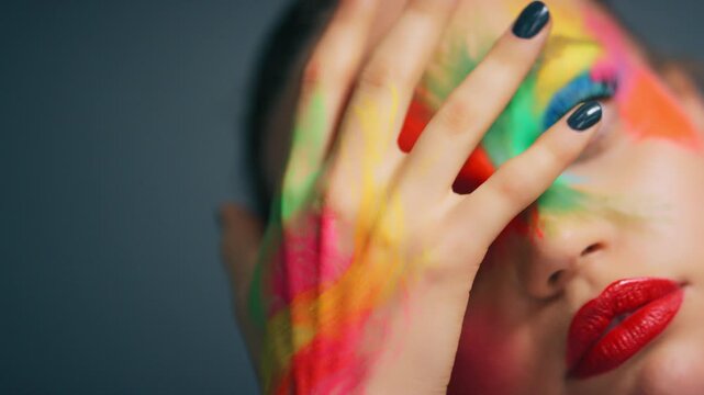 Face, art and woman with rainbow makeup, studio background or beauty aesthetic with colorful fantasy. Serious, person and self expression with red lipstick, paint and creative with cosmetics and glow