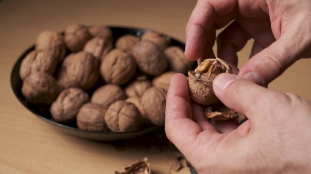 Hands cracking open a walnut over a bowl food preparation close up