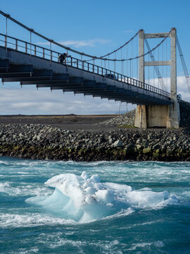 Photographer on the bridge carrying route 1 over Glacier Lagoon in Iceland with icebergs floating underneath