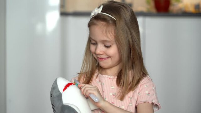 Little happy girl brushes teeth of toy shark with toothbrush. Toothless child. Baby milk teeth change. Oral hygiene. Health care