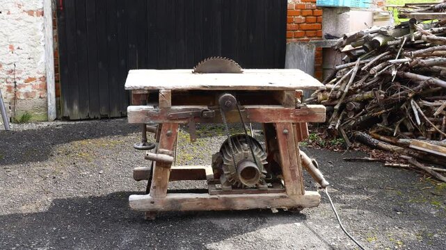 Old homemade circular saw in a wooden frame, showing rustic construction, industrial character, and traditional woodworking equipment used for cutting firewood in a rural workshop setting