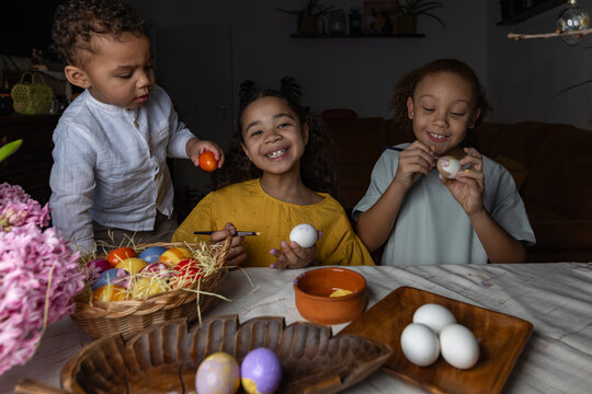 Siblings painting Easter eggs together at home in a festive spring setting