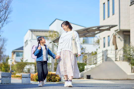 住宅街を手を繋いで歩く母親とランドセルを背負った女の子