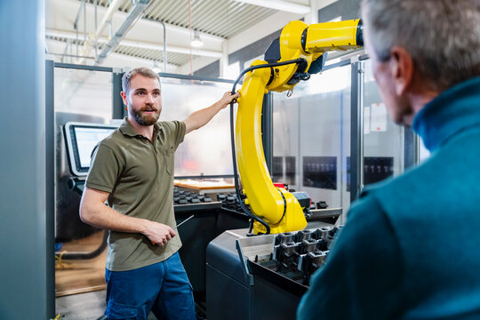 Two men discussing in a production hall with an industrial robot