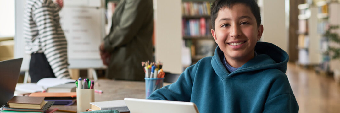 Boy smiling while studying with a tablet in a classroom setting