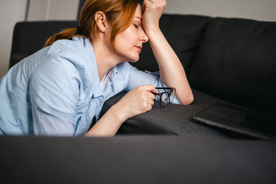 Exhausted woman feeling burnout at home with laptop and sofa