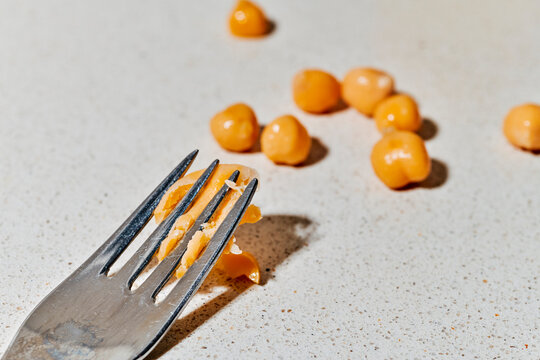 Cooked chickpea on kitchen countertop with fork crushing legume