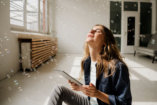 Creative woman enjoying bubbles with tablet in sunlit studio