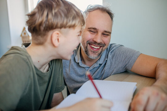 Father and son at home smiling while doing homework and learning
