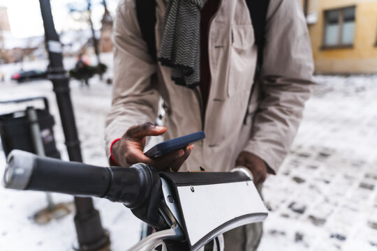 Man using smartphone for urban bicycle sharing in winter city