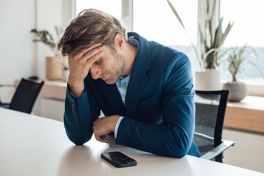 Stressed business professional in suit sits at office desk with phone