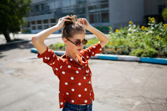 Woman with curly hair in red polka dot blouse styling hair outdoors