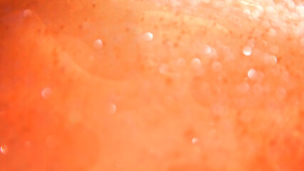 Fototapeta premium Defocused blurred bokeh background of water with paint particle texture in soft orange tones. Concepts for beauty and cosmetology, food and beverage industry, holidays and event designs, advertising.
