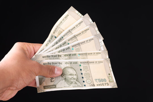 Close-up of hand holding a stack of new Indian 500 rupee currency notes on white background, Wealth and Finance concept.
