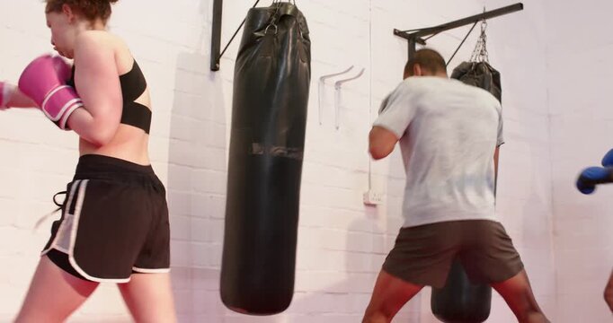 After warmup diverse boxers punching bags with boxing gloves, rotating stations at gym for fitness