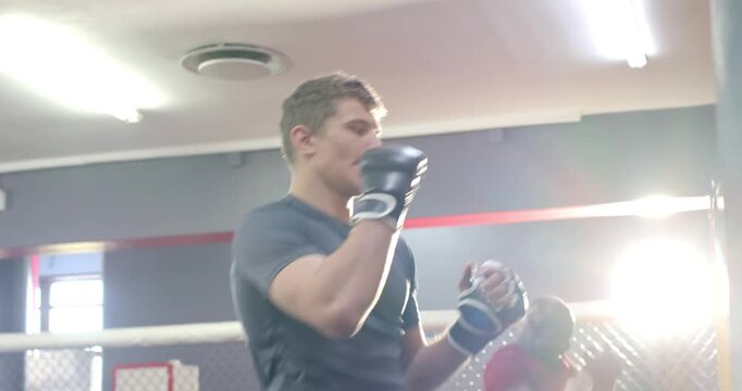 African American coach nodding to White trainee, coaching jabs on yellow punching bag in MMA cage