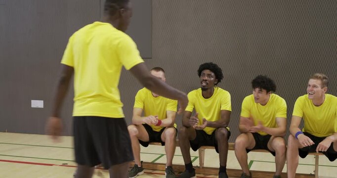 Yellow-shirted men rising and clapping after African American captain pointing and urging on bench